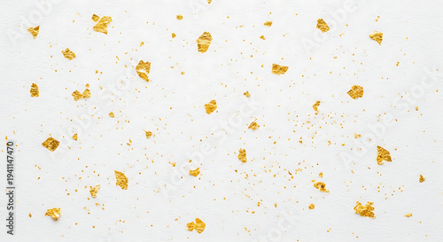 shimmering gold leaf flakes and scattered dust on a delicate white textured background creating an elegant luxury design.