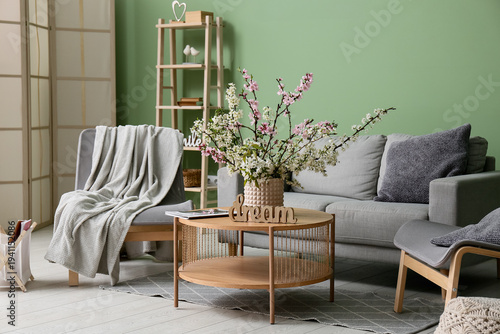 Sofa with armchairs, coffee table and vase of blooming branches near green wall in living room