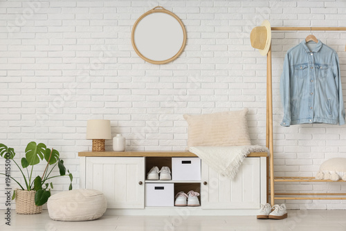 Bench and rack with clothes near white brick wall in interior of hallway