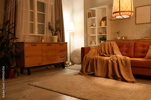 Interior of stylish living room with brown sofa, houseplants and glowing lamps at evening