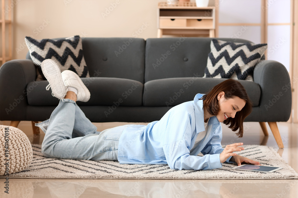 Obraz premium Young woman using modern tablet computer on carpet at home