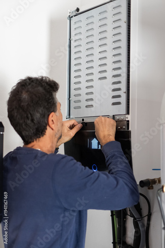 Man performing diy home maintenance, opening the cover of a modern heating system or boiler, troubleshooting or servicing the appliance in a utility room