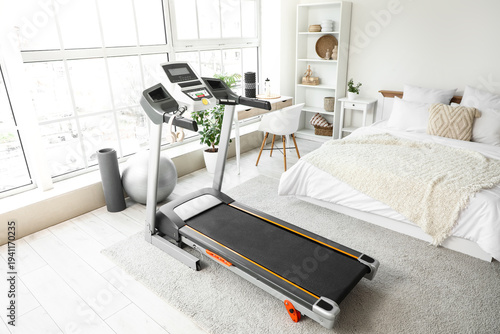 Interior of light bedroom with treadmill, tables and shelf unit