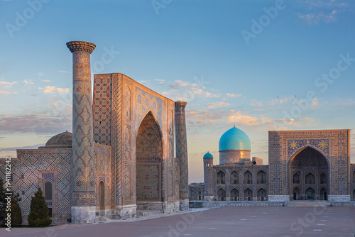 Ulugbek and Tillya Kari madrasa with turquoise dome at sunrise in gentle golden-pink rays of sun, clear blue sky. Ornate facade of timurid islamic architecture landmark Registan square, Uzbekistan.