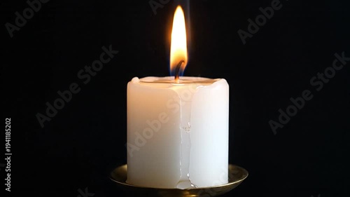 Serene white pillar candle with flame and dripping wax on dark