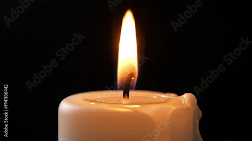 Closeup of a lit white candle with bright flame in darkness
