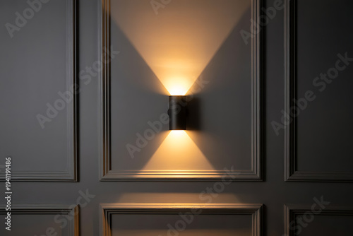 A modern black wall sconce illuminates a decorative gray paneled wall with a warm light pattern.