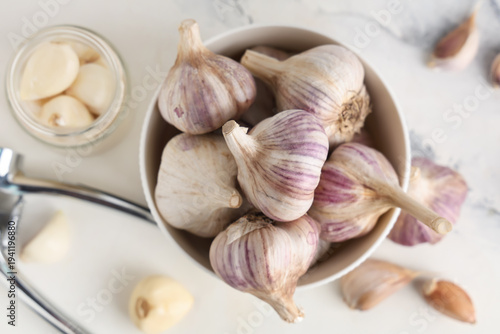 Bowl with fresh garlic and jar of cloves on white background