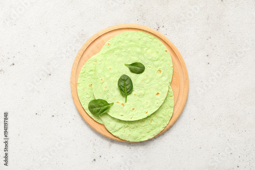 Wooden board with round green lavash and spinach on light grunge background