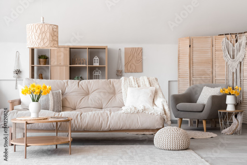 Interior of stylish living room with sofa, coffee table and vase of narcissus flowers