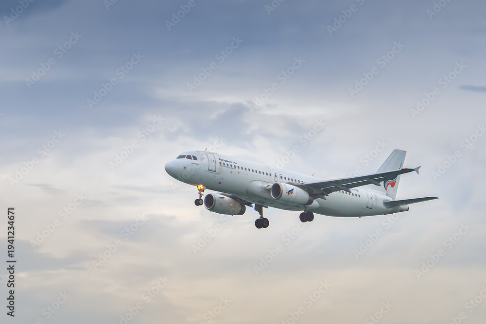 Fototapeta premium Phuket Thailand 25 11 2025: The Airbus A320-232 aircraft of the Thai airline Bangkok Airways flies with the landing gear extended against the background of the colorful sky.