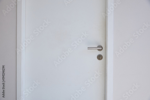 White door and door frame with steel handle on white concrete wall 