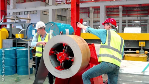 Workers are working on a production line in a sheet metal factory. An expert technician is overseeing the production control of metal sheets.
