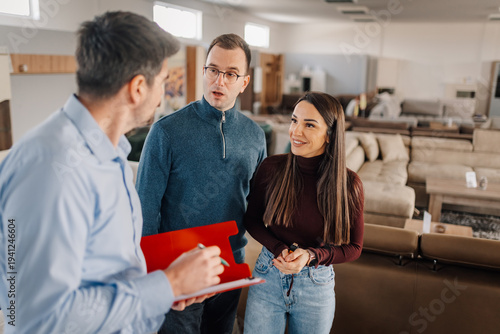 Salesman advising young couple choosing new furniture