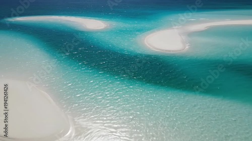 Aerial view of turquoise ocean water flowing around white sandy islands, creating beautiful patterns and textures in the water under bright sunlight
