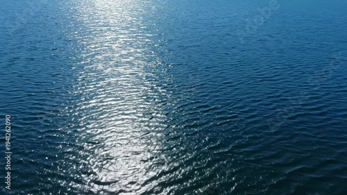 Sunlight reflecting on calm water surface, creating shimmering patterns and ripples, showcasing the tranquil beauty of a serene lake or ocean environment