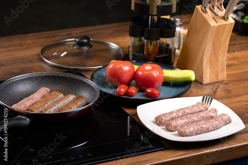 Traditional Balkan grilled minced meat dishes, kebapcheta and meatballs, being cooked in a frying pan in a home kitchen