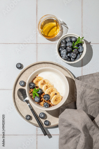 Greek yogurt with granola, blueberry and banana in a bowl on a blue tile background