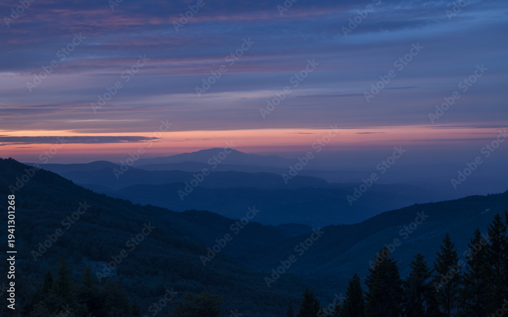 Naklejka premium Beautiful sunset over mountain peaks with warm golden light illuminating the landscape. Scenic natural view with dramatic sky, perfect for travel, adventure, and nature themes.
