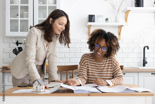 business person sitting at table, negotiating. two women are going through papers, discussing project. interior design, architectural bureau. diverse people, African American business woman realtor.