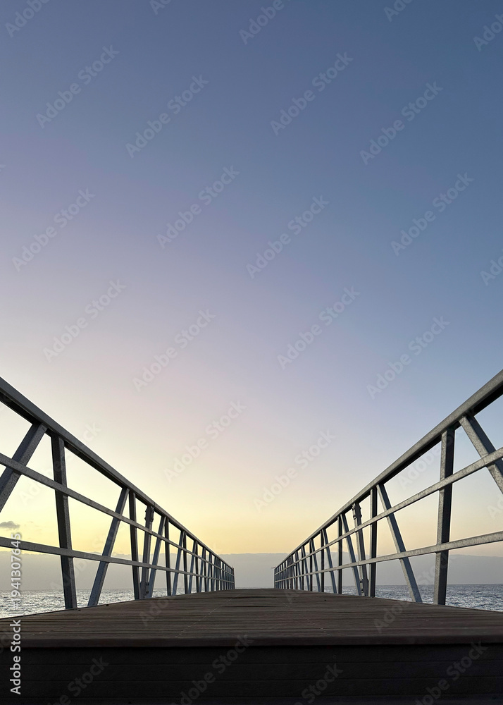Fototapeta premium The pier extending out over the water into a vast, pastel-colored sky at sunset.Powerful background for a reel about journey, reflection, or the beauty of nature.