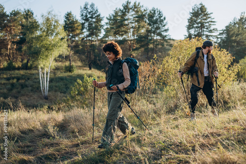 Black woman with partner walks as leans into Nordic walking poles
