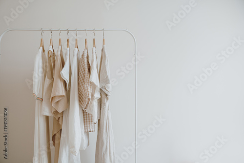 Various neutral-colored tops and blouses hanging on a white rack