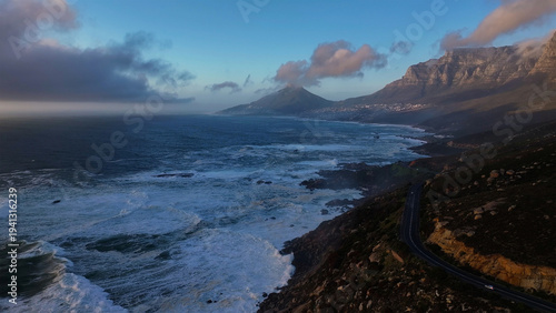 Aerial view of the dramatic coastline where the churning ocean meets the rugged cliffs beneath a sky of brooding clouds, Cape Town, Western Cape, South Africa.