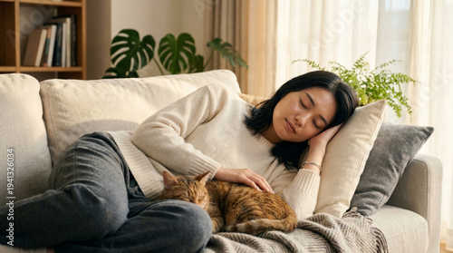 観葉植物のあるリビングのソファーで愛猫と寄り添って昼寝をする女性