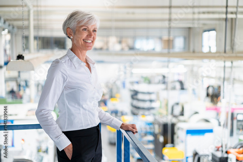 Smiling senior businesswoman on upper floor in factory overlooking shop floor