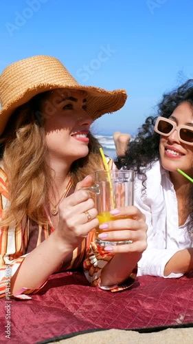 Two cheerful female friends drinking juice together at the beach