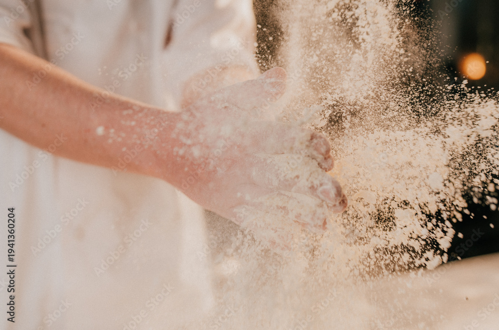 Fototapeta premium Hand smashes through white powder, creating a dynamic explosion. Dust particles float in warm, golden light. The motion suggests energy, creativity, or celebration