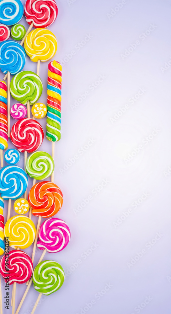 Obraz premium Array of colorful, spiral lollipop candies on wooden sticks, arranged on a pale purple background, symbolizing celebration, childhood joy, and sweetness
