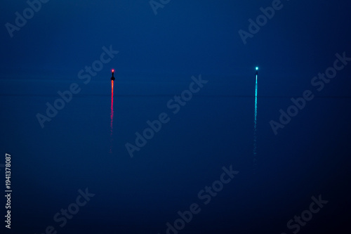 Two illuminated buoys on a calm sea surface at dawn, view of the North Sea or Jade Bay in the morning at the cross-range light, Alte Mole in 26382 Wilhelmshaven, Germany