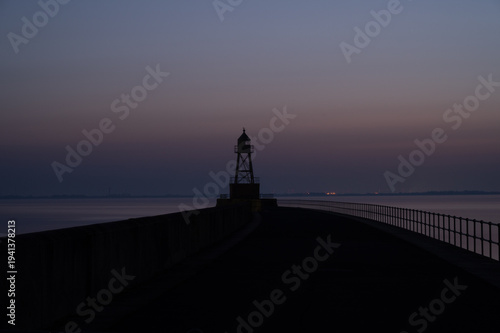 Silhouette of a lighthouse at dawn, surrounded by the sea and a railing, view of the North Sea or Jade Bay in the morning at the cross-range light, Alte Mole in 26382 Wilhelmshaven, Germany
