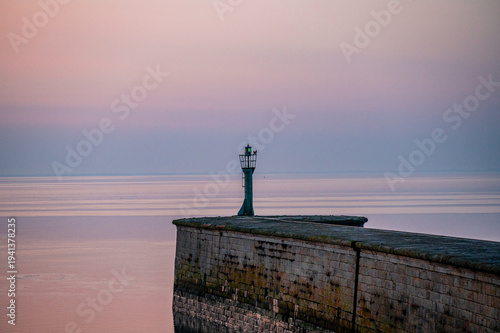 A lone lighthouse stands on a pier, the sea is calm and the sky is tinted in pastel colors, a view of the North Sea or Jade Bay in the morning at the former second entrance in 26382 Wilhelmshaven.