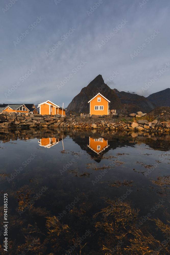 Obraz premium Stunning fall scenery in the Lofoten Islands. Iconic red rorbu cabins nestled between rocky coastlines and dark arctic waters during the golden hour. Travel Norway.