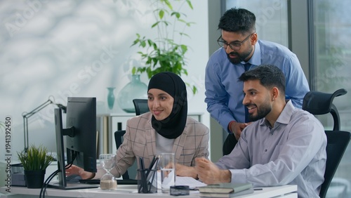 Excited smiling happy Arabian Muslim business team in office looking at computer online work job with pc internet teamwork motivation career partnership businesspeople working cooperating indoors
