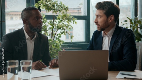 Two diverse businessmen multiethnic men business team at office with laptop talking negotiating Caucasian male manager consulting insurance African man listening cooperate conversation brainstorming