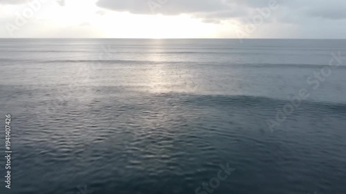 Serene ocean waves gently rolling towards the shore under a cloudy sky, reflecting soft light across the water surface in a tranquil coastal setting