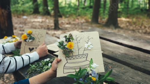 Canvas Print Children creating nature art with flowers and drawings on cardboard outdoors