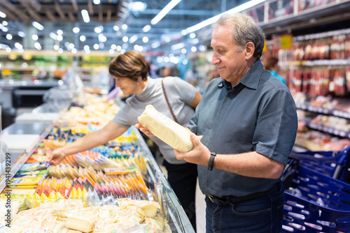 Canvas-taulu Elderly man choose cheese in supermarket