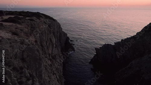 Aerial drone view flying along steep Atlantic cliffs carved by marine erosion on the Costa Vicentina coastline near Farol do Cabo Sardão in Odemira, Alentejo region of Portugal during sunset light.