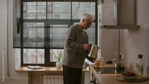 Side view medium long shot of senior Caucasian man in eyeglasses making drip coffee in modern kitchen, pouring hot water from electric kettle into two mugs and walking away