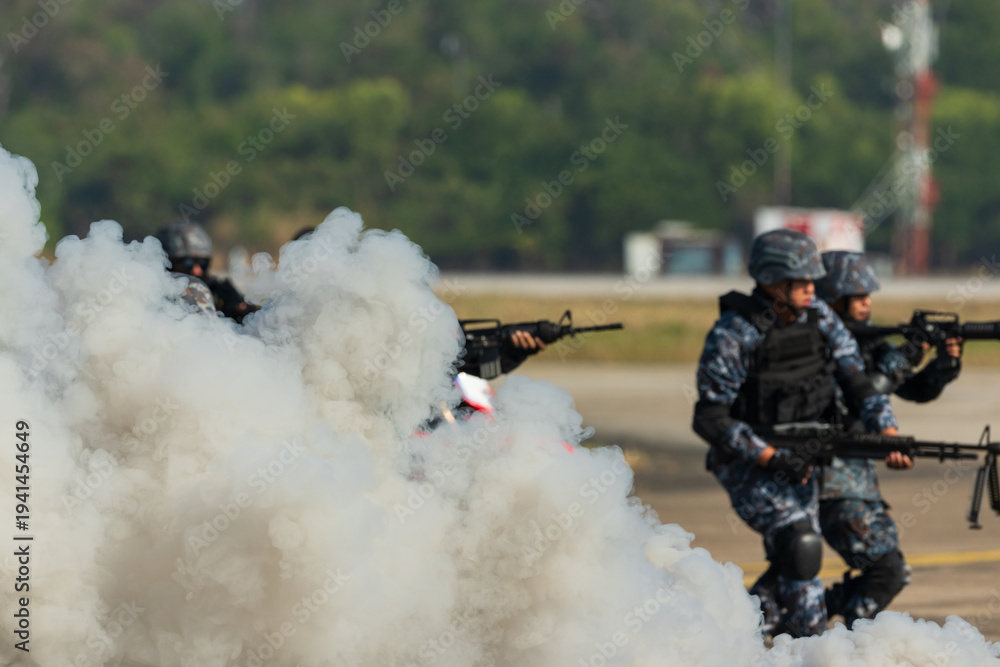 Naklejka premium Smoke from smoke bomb and military personnel walking on the road.Group of military men holding gun.Soldiers in military uniform with machine guns training on the battlefield.