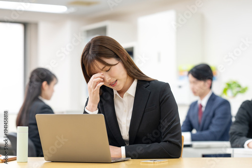 仕事中に頭痛や疲れを感じて悩むビジネスパーソン　オフィス・残業・ストレス