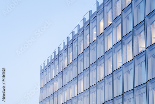 View of a modern building with symmetrical glass windows reflecting the soft blue sky, creating a serene and minimalist urban scene, Oslo, Norway.