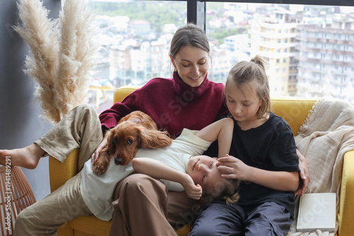 Happy mother and children sitting on couch with his puppy dog pet. Loving family at home