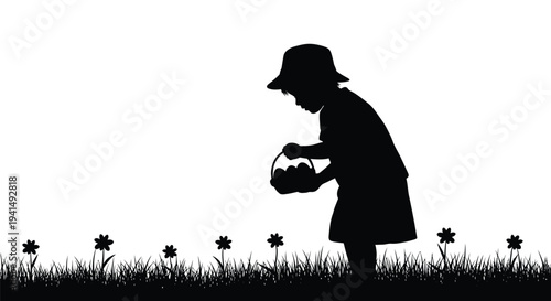 Young child in a hat collecting Easter eggs in a basket from grassy ground with flowers.