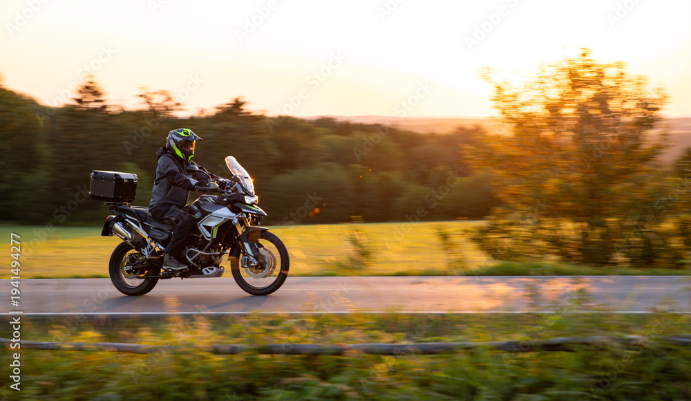 Fototapeta premium Driver riding motorcycle on empty road during sunset, spring mountains